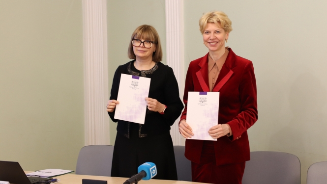 Attēlā redzama profesore Linda Daniela un izglītības un zinātnes ministre Anda Čakša, kas tur rokās mapes ar IZM logotipu