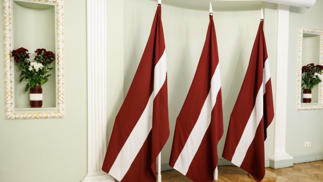 Trīs Latvijas karogi un ziedu kompozīcijas Latvijas Valsts svētku krāsās.