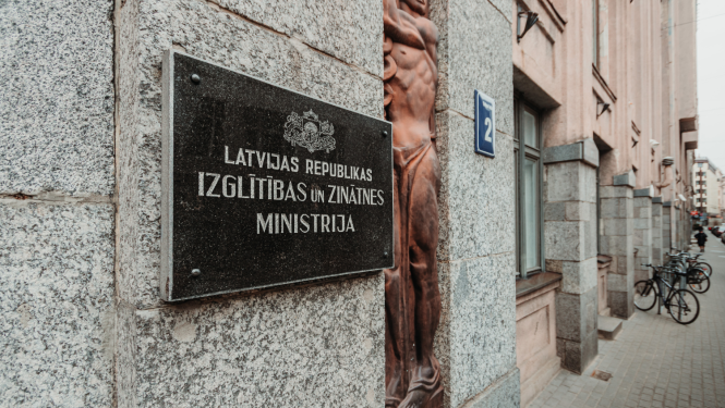 Izglītības un zinātnes ministrijas ieejas durvis, pie sienas plāksne ar IZM logo un uzrakstu
