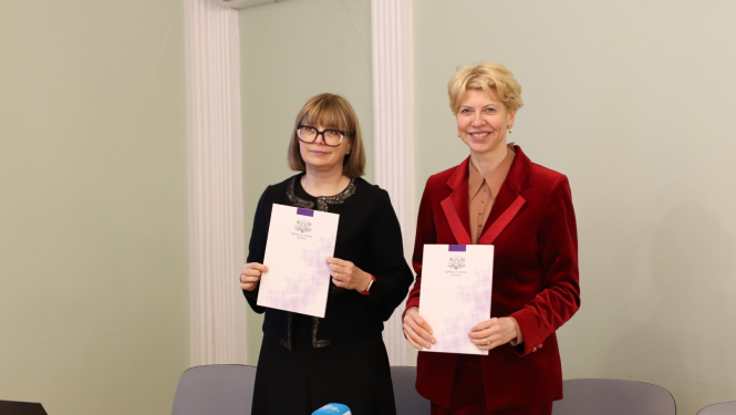 Attēlā redzama profesore Linda Daniela un izglītības un zinātnes ministre Anda Čakša, kas tur rokās mapes ar IZM logotipu