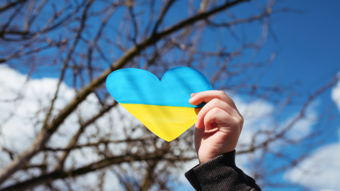 Cilvēka rokas, kas tur papīra sirdi Ukrainas karoga krāsās 