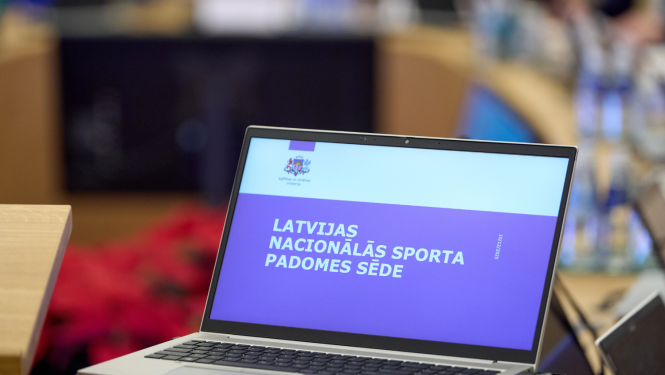 Ministru kabineta sēžu zālē stāv dators ar atvērtu IZM prezentāciju, kur rakstīts "Latvijas Nacionālās sporta padomes sēde"