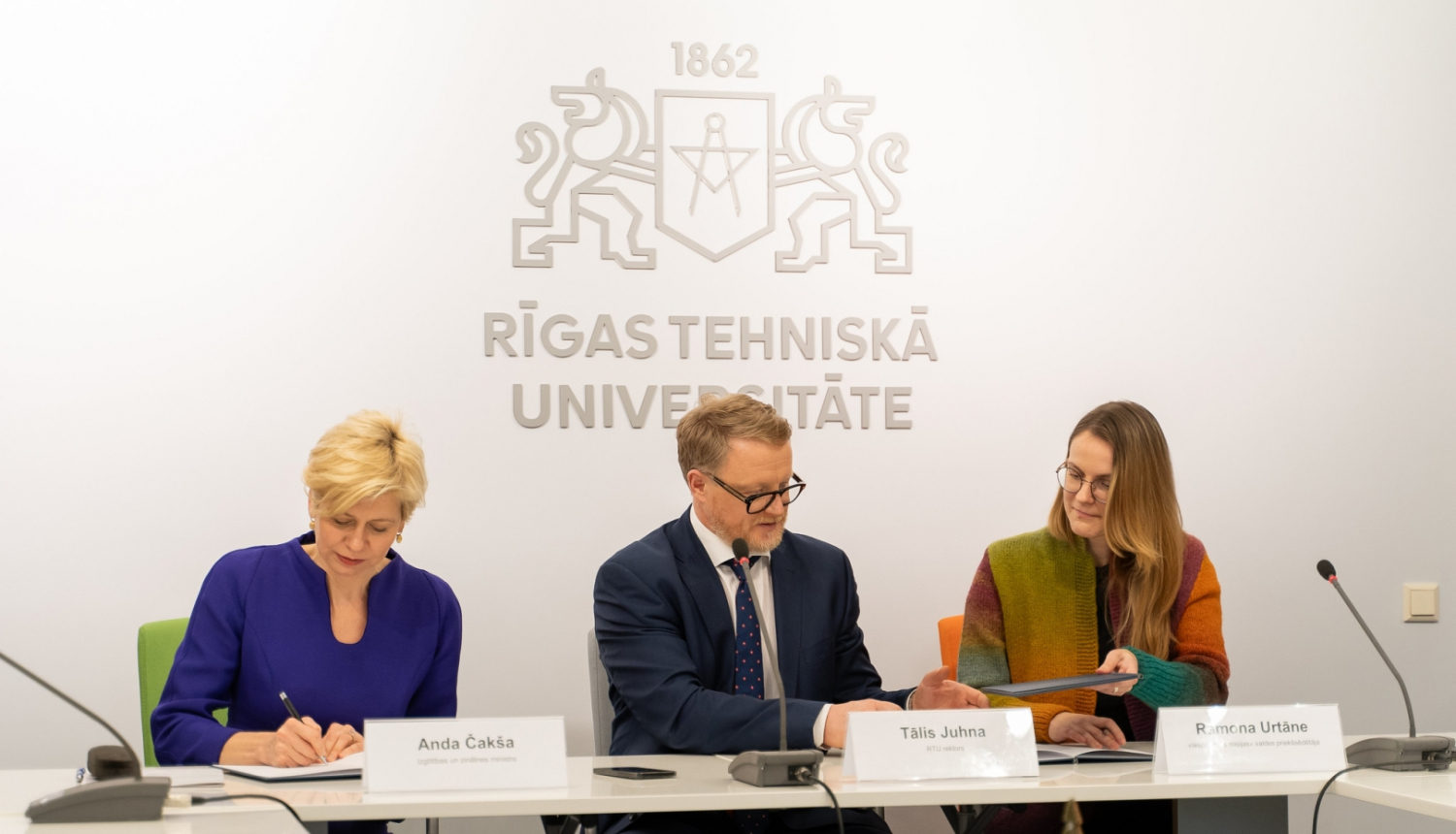 Anda Čakša, Tālis Juhna un Ramona Urtāne sēž pie galda memoranda parakstīšanā