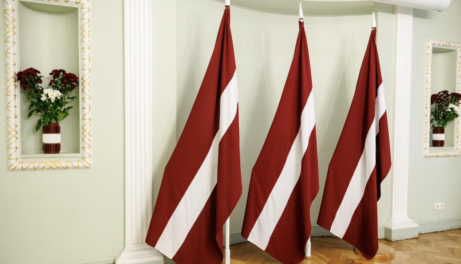 Trīs Latvijas karogi un ziedu kompozīcijas Latvijas Valsts svētku krāsās.