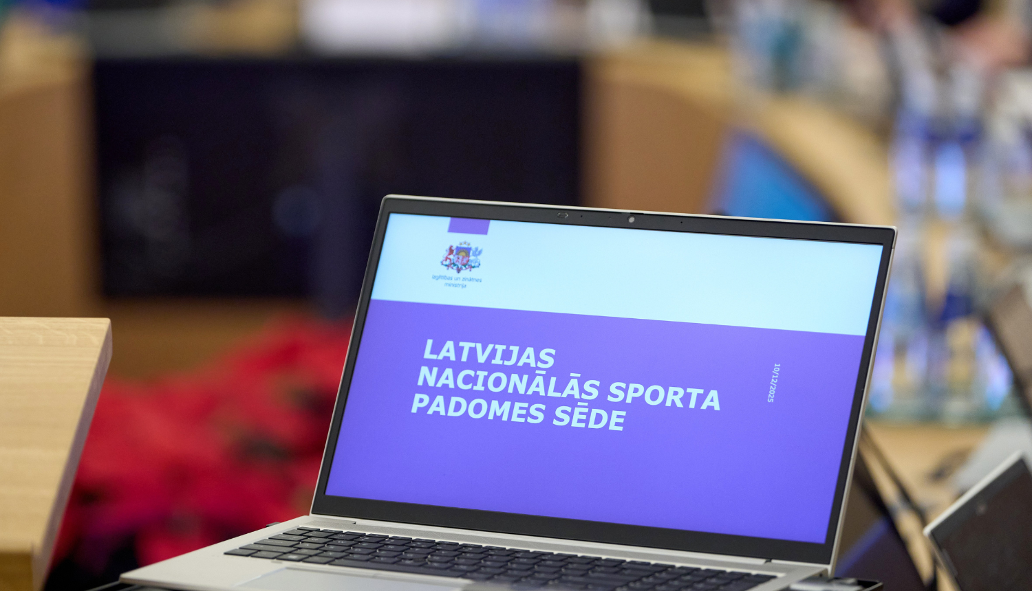 Ministru kabineta sēžu zālē stāv dators ar atvērtu IZM prezentāciju, kur rakstīts "Latvijas Nacionālās sporta padomes sēde"