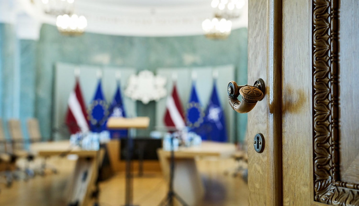 Pavērtas durvis uz ministru kabineta sēžu zāli, redzami Latvijas, Eiropas Savienības un NATO karogi fonā