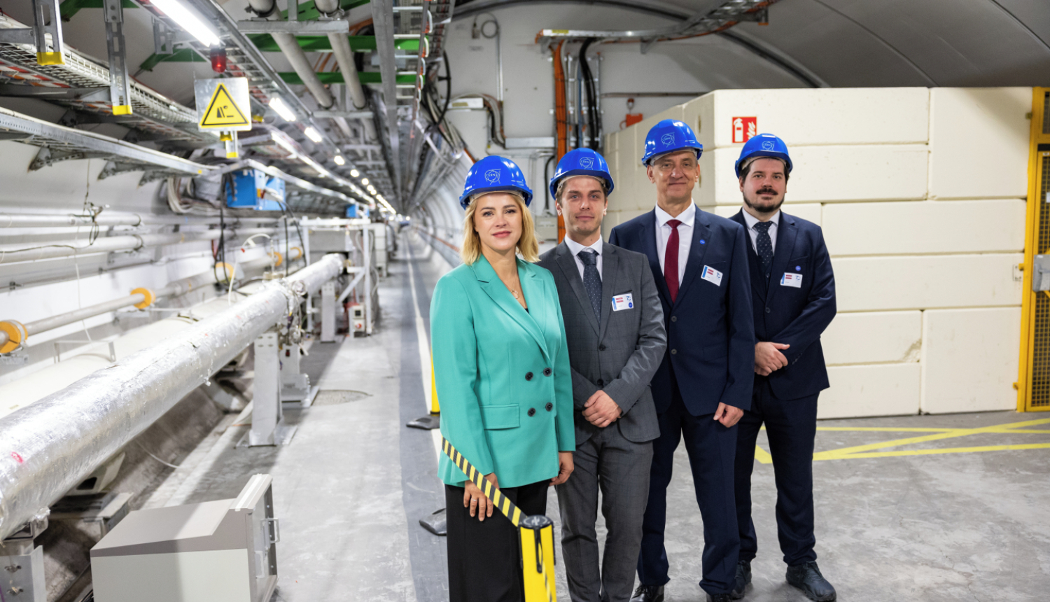 Premjerministre Evika Siliņa un citi Latvijas delegācijas pārstāvji zilās ķiverēs stāv CERN telpās.