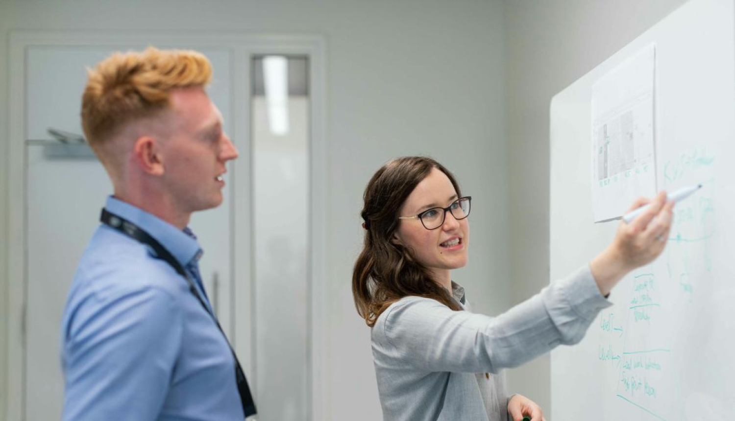 A woman writes on a blackboard, explains information to a man. The image is for illustrative purposes only..
