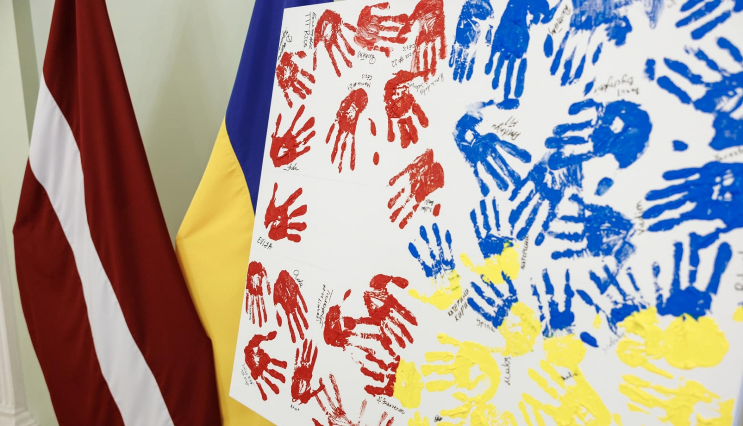 Latvijas un Ukrainas karogi, priekšplānās balts audekls ar krāsā iemērktiem rokas nospiedumiem sarkanā, zilā un dzeltenā krāsā