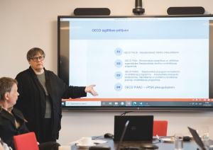 Lektore stāsta semināra auditorijai, aizmugurē ekrāns