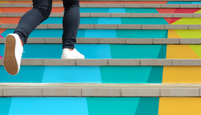 Cilvēks skrien augšā pa kāpnēm, kāpnes nokrāsotas dažādās krāsās. 