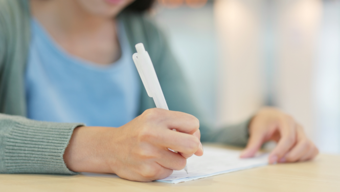 Meitene raksta ar baltu pildspalvu, fokuss uz roku