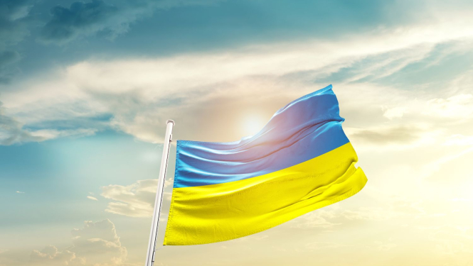 Ukrainas karogs plīvo vējā uz saulrieta fona