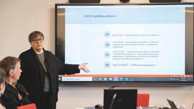 Seminārā Aija Zobena stāsta, fonā liels ekrāns ar prezentāciju