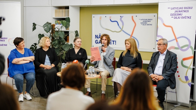 XIII Latvijas Skolu jaunatnes dziesmu un deju svētku preses konference. Skats no zāles, priekšā sēž seši cilvēki un stāsta par pasākuma norisi.