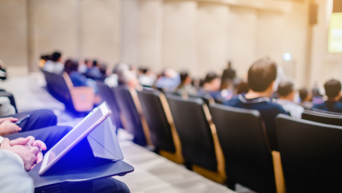 Auditorija ar studentiem, uz galda stāv planšetdators.