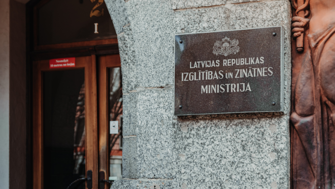 Izglītības un zinātnes ministrijas ieejas durvis, pie sienas plāksne ar IZM logo un uzrakstu