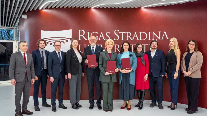 RSU un IZM pārstāvju kopbilde pie sienas, kur redzams Rīgas Stradiņu universitātes logo.