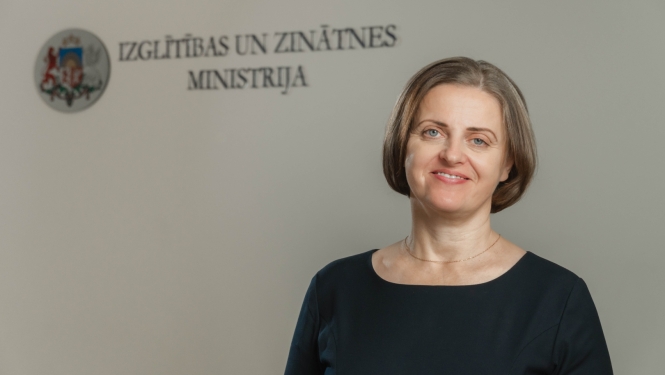 Edīte Kanaviņa, fonā Izglītības un zinātnes ministrijas logo