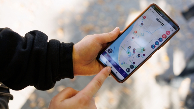 Jaunieša rokas tur rokās telefonu, kura ekrānā ir karte ar atzīmētiem apskates objektiem