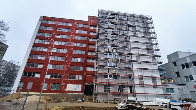 Attēlā redzama Rīgas Tūrisma un radošās industrijas tehnikuma dienesta viesnīcas fasāde - 9 stāvus augsta ēka, daļa ir sarkanā krāsā, daļa pelēkā, sarkanā daļa ir vēl ar veco apmetumu, pelēkā daļa ir sagatavota rekonstrukcijai. 
