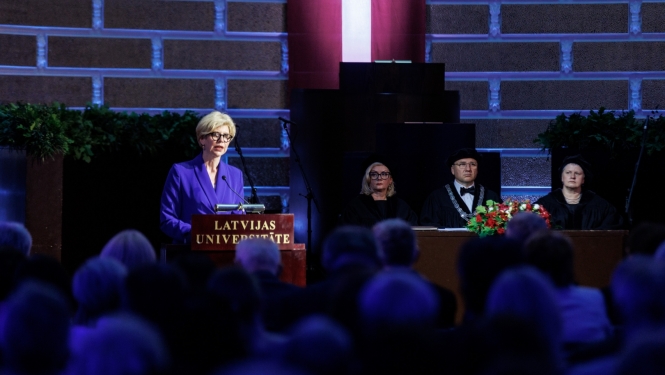 Izglītības un zinātnes ministre Anda Čakša saka uzrunu LU Lielajā aulā, fonā Latvijas karogs