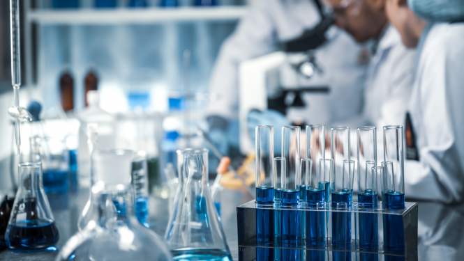 Zinātnieki strādā laboratorijā, priekšplānā mēģenes ar zilu šķidrumu 