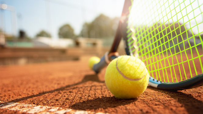 Tenisa bumbiņa un tenisa raķete noliktas uz zemes
