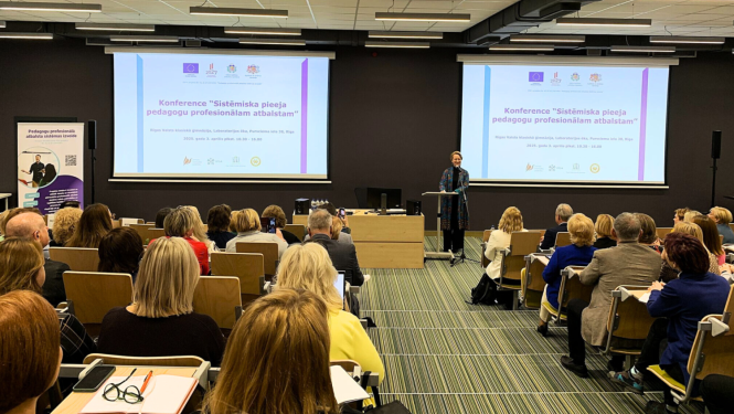 Cilvēku grupa sēž un klausās konferenci. Konferenci atklāj izglītbas un zinātnes ministre Dace Melbārde.