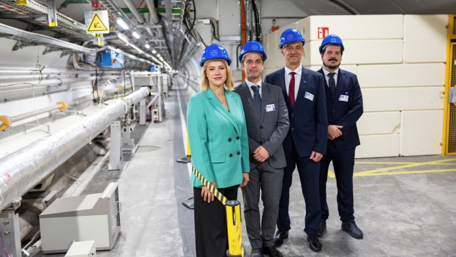 Premjerministre Evika Siliņa un citi Latvijas delegācijas pārstāvji zilās ķiverēs stāv CERN telpās.