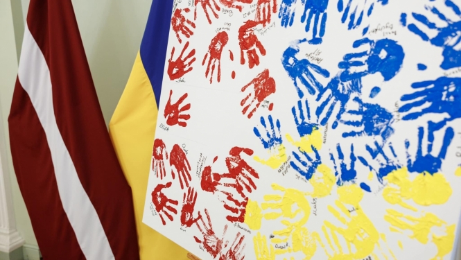 Latvijas un Ukrainas karogi, priekšplānās balts audekls ar krāsā iemērktiem rokas nospiedumiem sarkanā, zilā un dzeltenā krāsā