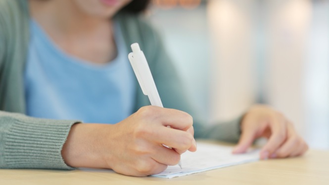 Meitene raksta ar baltu pildspalvu, fokuss uz roku