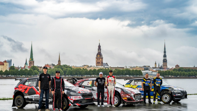 Fonā Rīgas ainava, priekšplānā 3 rallija mašīnas un pie katras stāv 2 sportisti