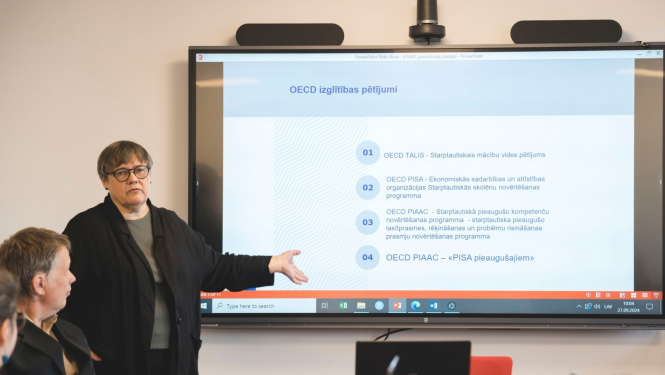 Seminārā Aija Zobena stāsta, fonā liels ekrāns ar prezentāciju