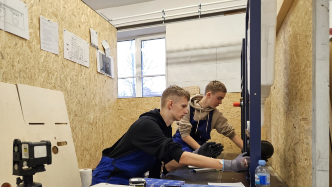 Divi puiši skrūvē instalāciju, apkārt skaidu plākšņu sienas