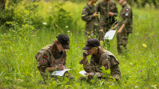 Divas meitenes formastērpos sēž pļavā ar rāciju un karti