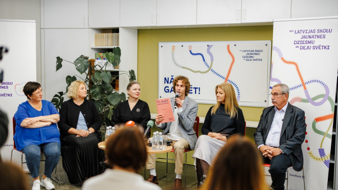 XIII Latvijas Skolu jaunatnes dziesmu un deju svētku preses konference. Skats no zāles, priekšā sēž seši cilvēki un stāsta par pasākuma norisi.