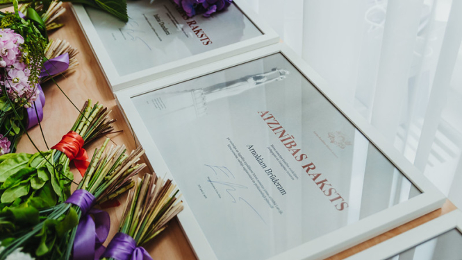 Ministru kabineta Atzinības raksti. Blakus stāv puķu pušķi.