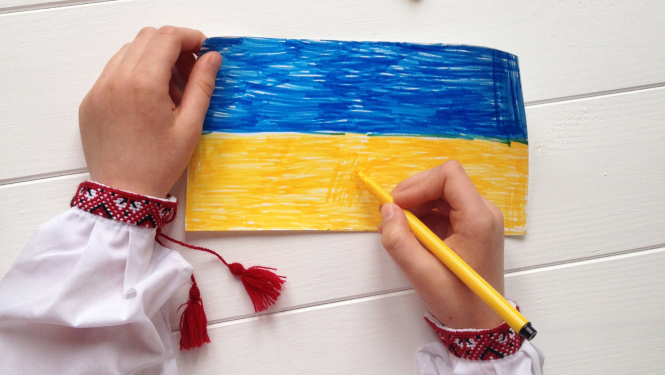 Bērna rokas, bērns krāso Ukrainas karogu.