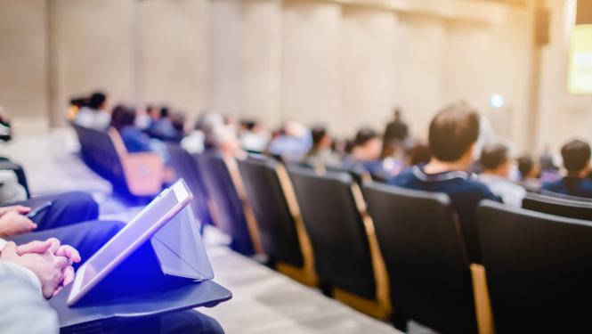 Auditorija ar studentiem, uz galda stāv planšetdators.