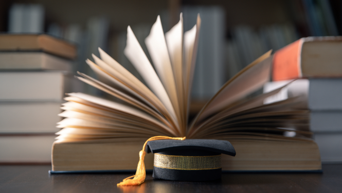 Uz galda stāv grāmatas un absolventu cepure.