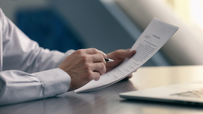 Cilvēks tur rokās dokumentu un pildspalvu.