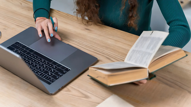 Sieviete strādā pie datora, rokā tur grāmatu.
