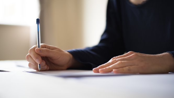 Cilvēks tur rokās pildspalvu un raksta papīra lapā.
