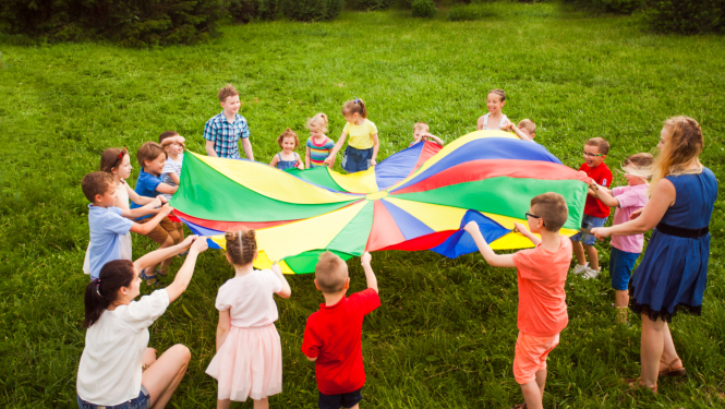 Bērni spēlējas pļavā ar spēļu izpletni