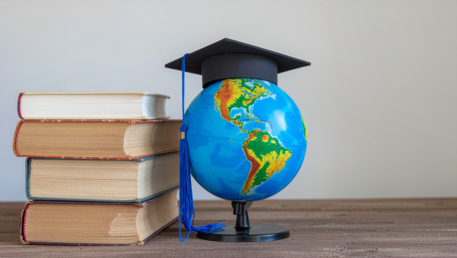 Uz galda stāv grāmatas uz globuss, uz globusa absolventa cepurīte