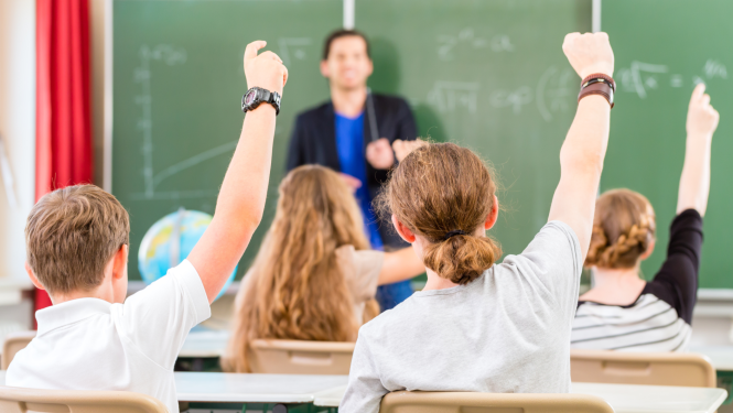 Skolēni pacēluši rokas, skolotājs stāv pie tāfeles
