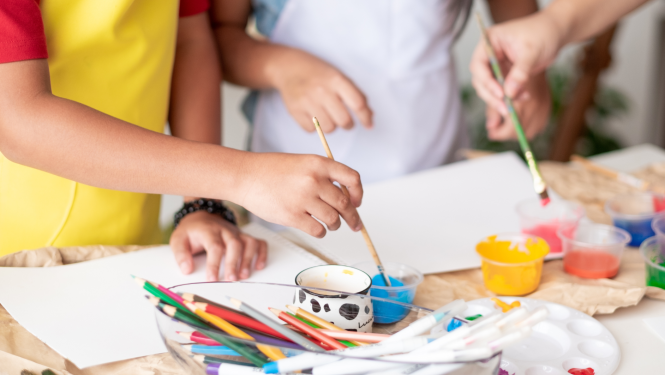 Bērni glezno, uz galda stāv zīmuļi un krāsas