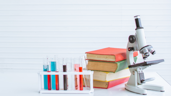 Uz galda stāv mēģenes, grāmatu kaudze un mikroskops