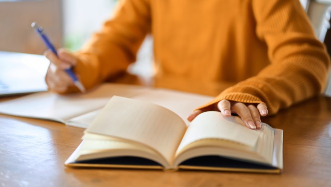 Cilvēks veic pierakstus kladē un pēta grāmatu